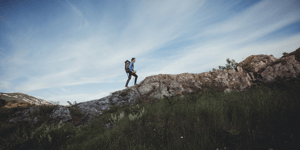 man hiking up mountainside with backpack 