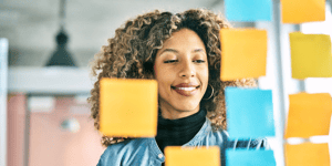 woman looking at glass wall with yellow and blue sticky notes on it