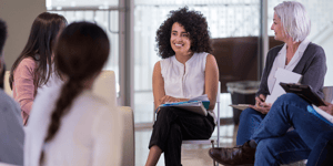 group of individuals sitting in a circle talking and smiling