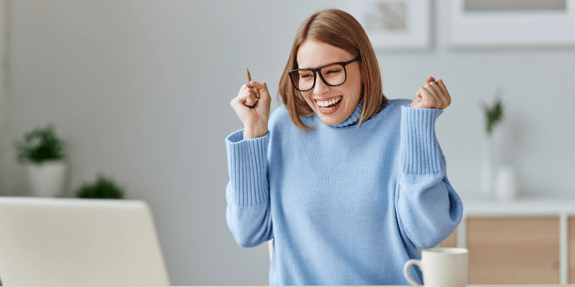 woman in blue sweater excited while working on a laptop