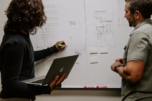 two individuals writing on whiteboard