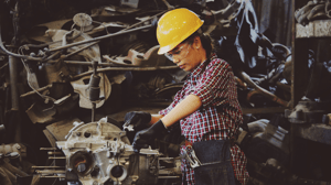 woman in manufacturing wears yellow hard hat while working on automotive part