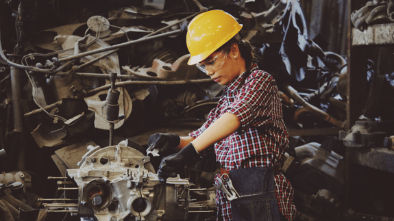 woman in manufacturing wears yellow hard hat while working on automotive part
