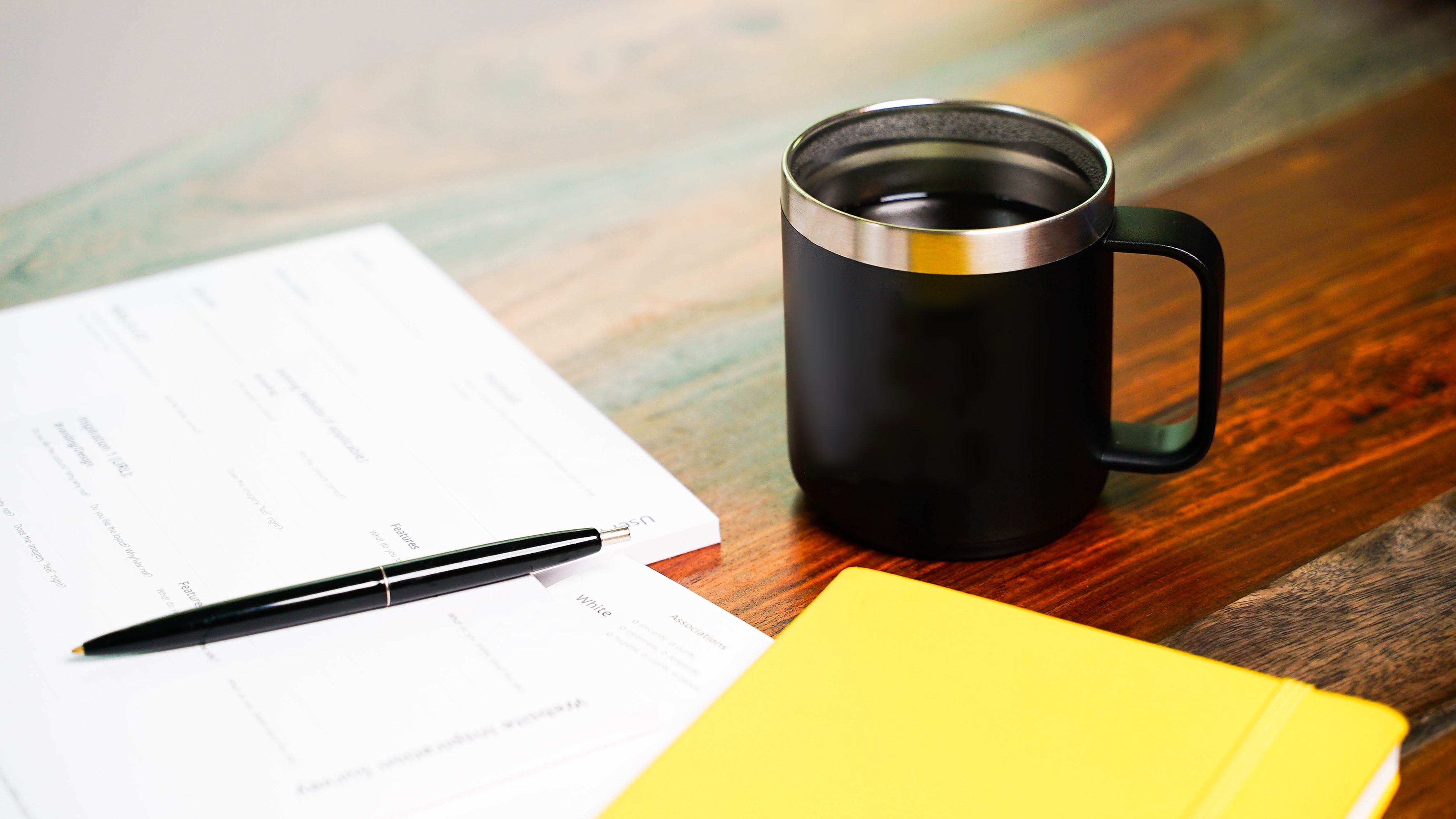 wood desk with open notepad, pen, and coffee mug